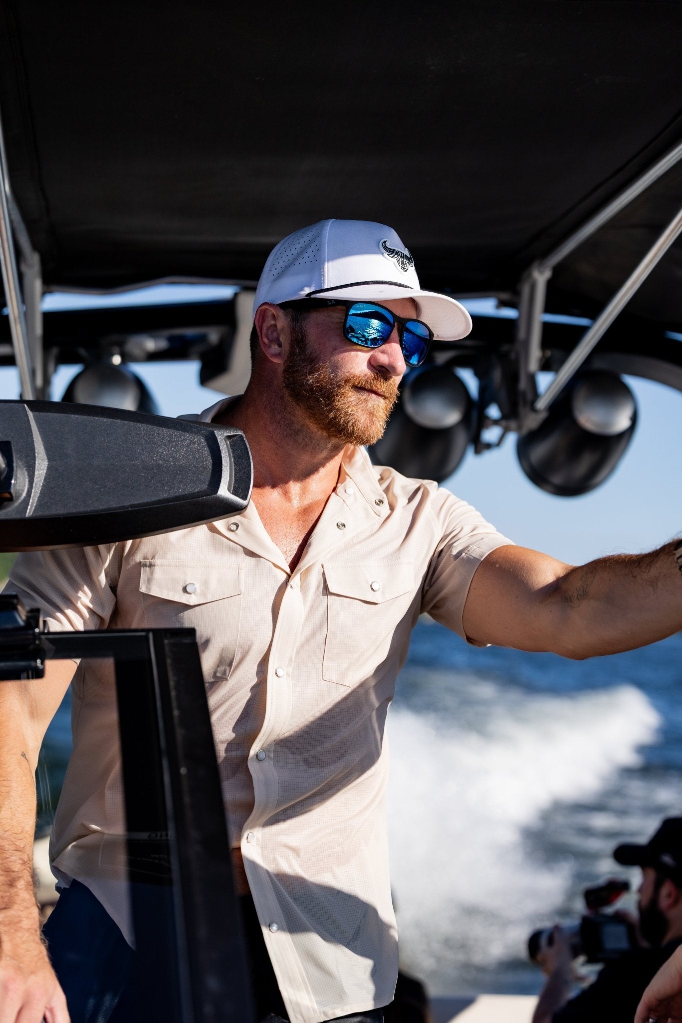 Man driving a boat, wearing a cream colored pearl snap shirt.