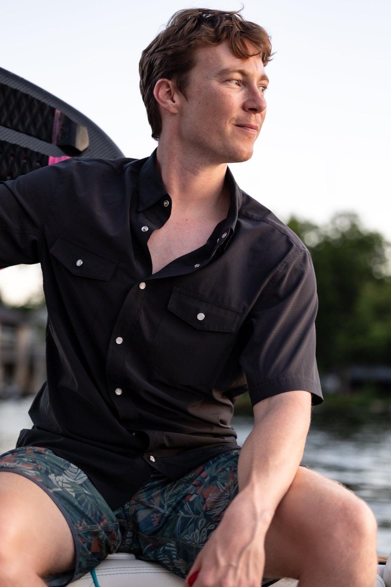 Man sitting on a boat wearing a black pearl snap shirt.